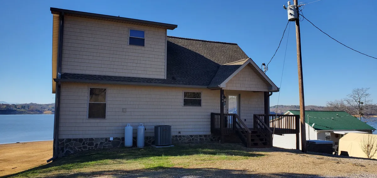 A broad exterior perspective of the home's facade, deck area, and a beautiful lake view beyond. The tranquil mood highlights the connection between indoor comfort and outdoor serenity—ideal for enjoying morning coffee, evening stargazing, or simply savoring the natural landscape.