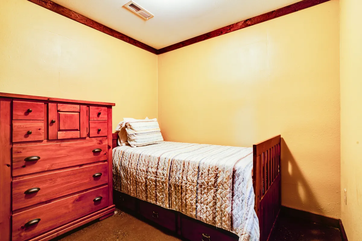 A calm and tidy room featuring a single bed with fresh bedding and a wooden dresser. The simplicity and coziness of the space are suited to a child's or guest bedroom, supporting restful nights and intimate conversations.
