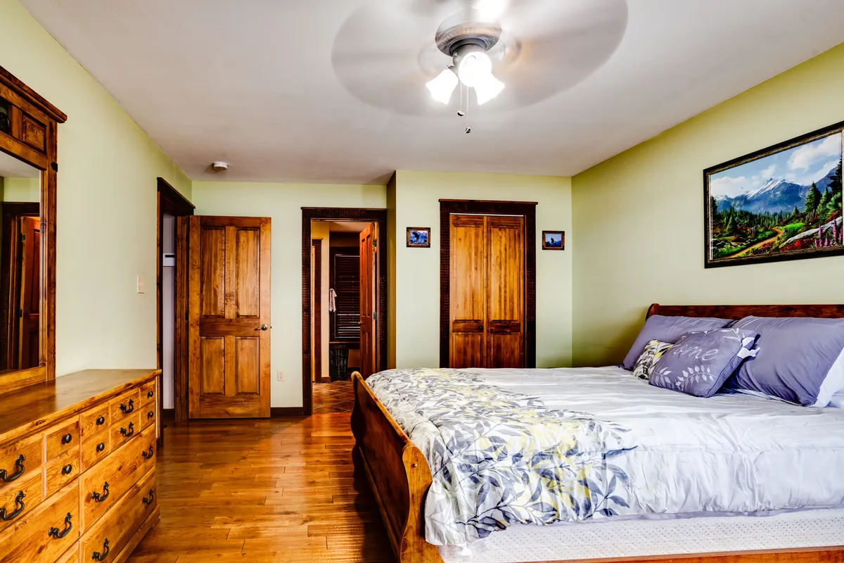 An inviting bedroom with a cozy bed, dresser, decorative painting, and doors leading to another space. The ambiance is warm and conducive to relaxation, suggesting a private sanctuary for restful nights or lazy mornings.