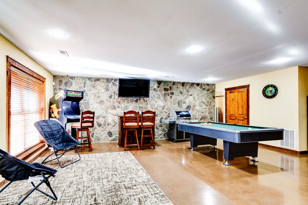 A fun, casual game room with a pool table, bar seating, an arcade machine, stone wall, and a TV. The space is vibrant and designed for entertainment, but also features a futon for flexible sleeping arrangements.