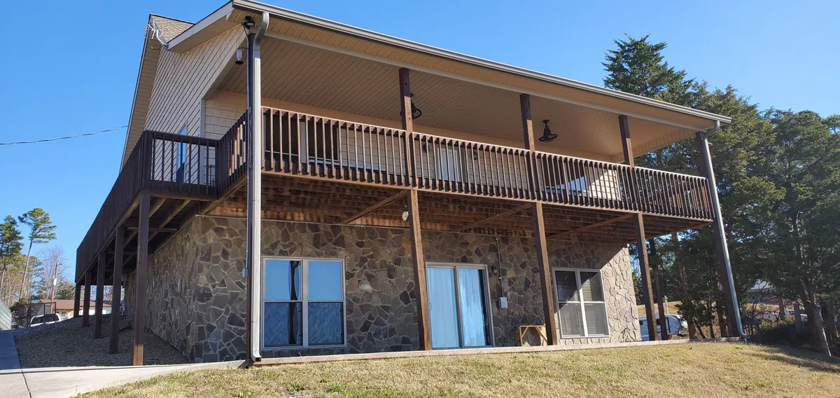A wide exterior view of the home’s balcony and stone facade, featuring double doors and ample space for gatherings. The image conveys a welcoming, social atmosphere with sunset lighting enhancing the warmth of the setting.