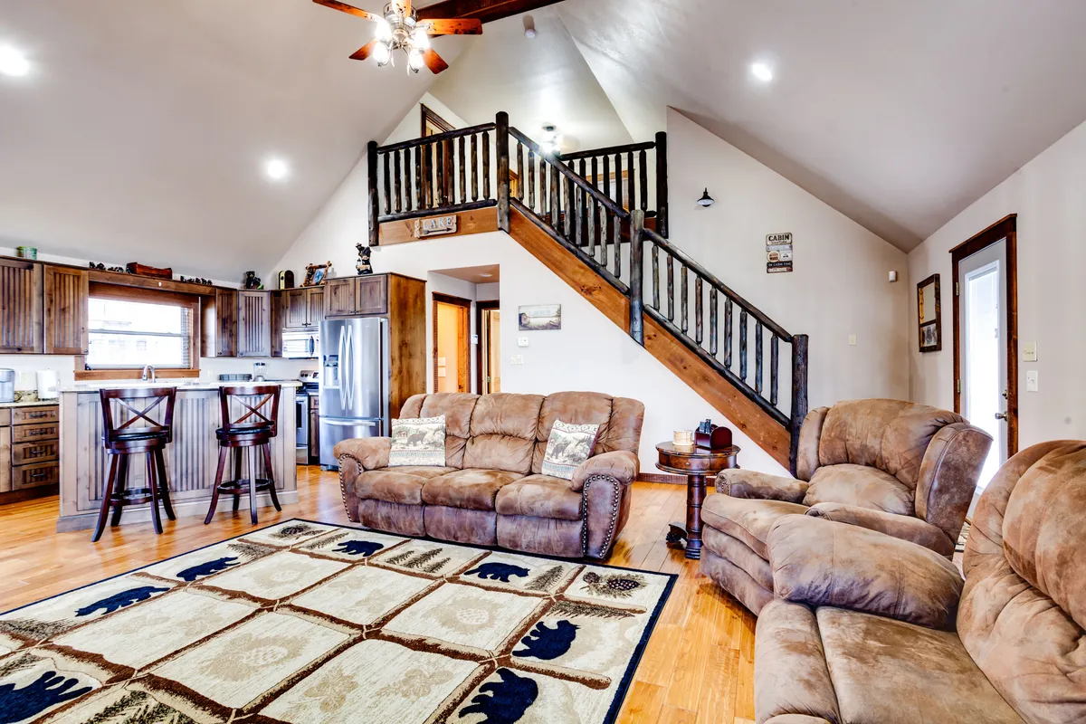 This interior image highlights a spacious open-concept living area featuring a plush sofa seating arrangement, a visible kitchen area with a breakfast bar, and an area rug—all set beneath ample natural light. The space invites relaxation and fosters social gatherings, perfectly illustrating communal living.