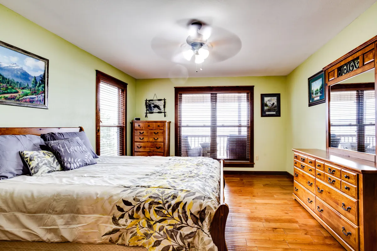 A calm and peaceful bedroom featuring a king-size bed, a wooden dresser, tasteful artwork on the walls, and a window with blinds letting in gentle sunlight. The space feels inviting and restful, perfect for unwinding after a busy day.