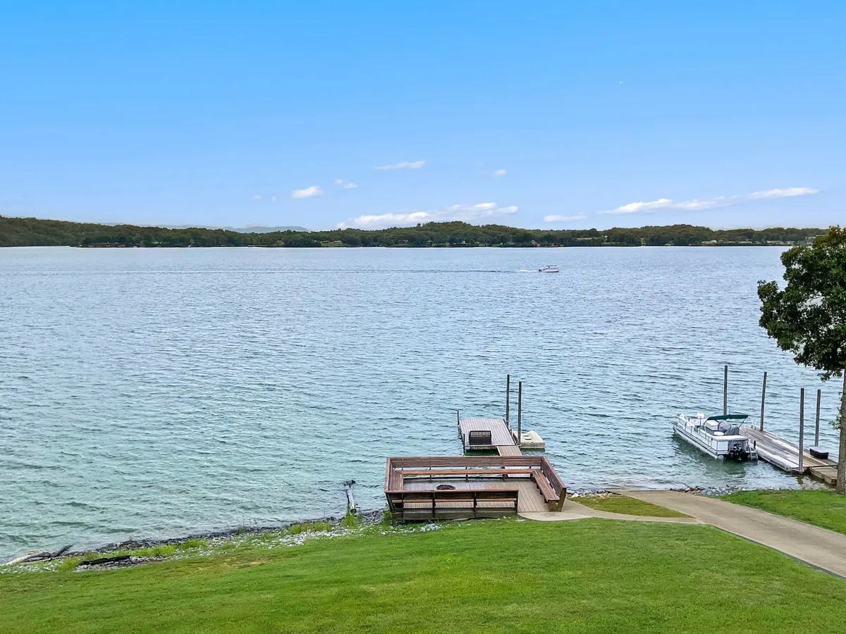 This serene view focuses on the lake, docks, and a lush green lawn. The tranquil waters and visible dock reinforce the idea of launching boats directly from the property, fishing, or relaxing by the shore. The setting sun adds warmth and hints at memorable evening gatherings by the water.