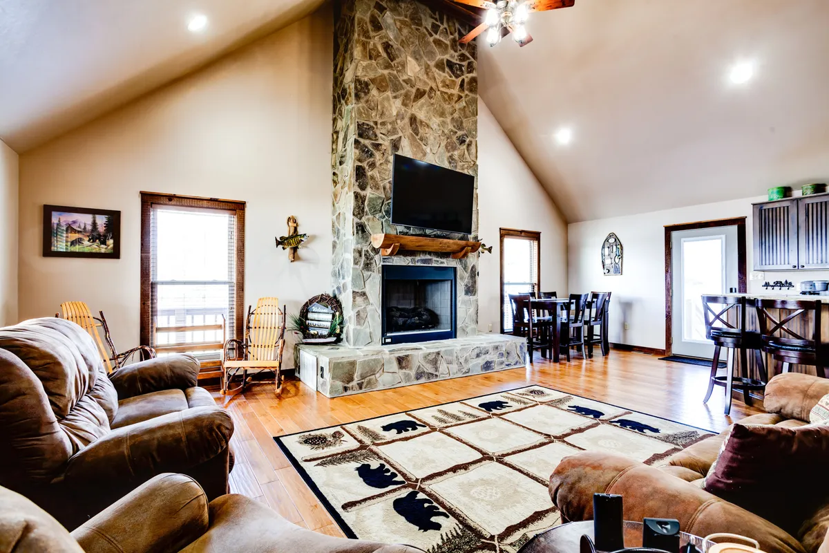 A spacious living room with a prominent stone fireplace, comfy sofas, a large TV, and an area rug. The setup suggests a cozy environment for family gatherings or unwinding after a day spent exploring nearby attractions.