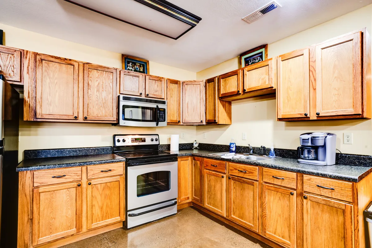 This image focuses on a fully equipped kitchen with stainless steel appliances, wooden cabinetry, and a sleek black countertop. The area is functional and inviting, ideal for meal prep and serving snacks during gatherings or game nights.