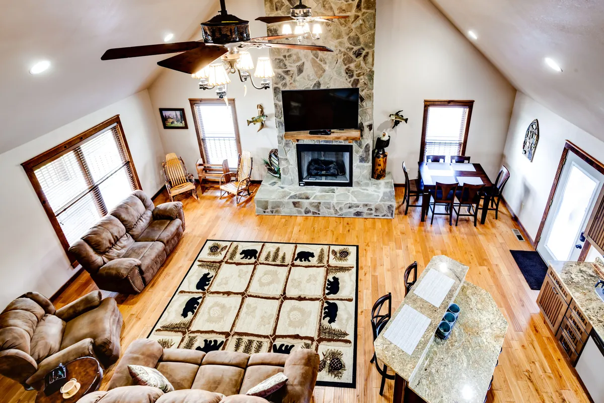 A beautifully appointed living and dining area where a stone fireplace serves as a cozy focal point. Comfortable seating, a large rug, and an adjacent dining area flow into the kitchen island, capturing the seamless connection between living, dining, and kitchen spaces.