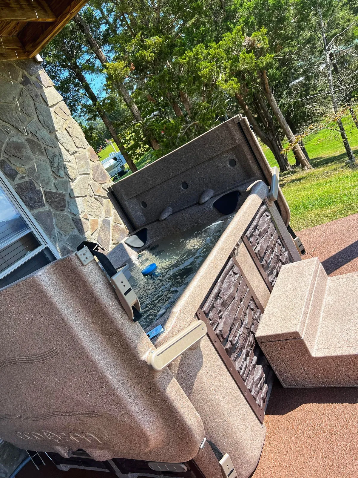 A soothing outdoor scene featuring a private hot tub nestled among greenery on a spacious patio. The hot tub area is surrounded by nature, offering a tranquil setting for relaxation after a day of lakeside activities.