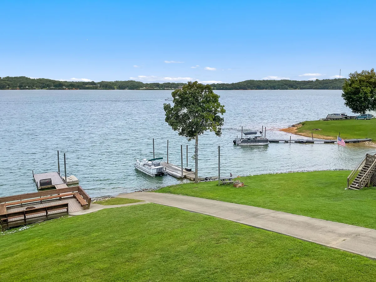 This image captures a broad, tranquil view of the lake with boats, a green lawn, a tree, and visible docks. It suggests a place where one can boat, fish, picnic, swim, or simply relax by the water. The expansive perspective emphasizes the direct lakefront access described in the section and hints at the variety of water-based activities available.