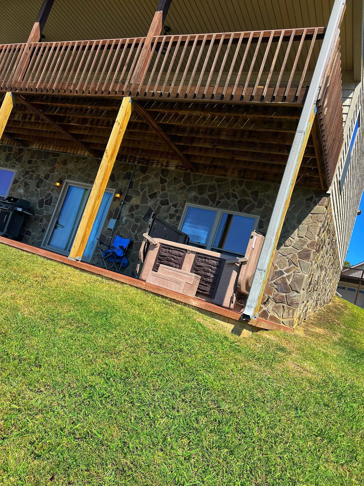 This image features a hot tub on a balcony overlooking a tranquil landscape, with a stone wall and wood accents framing the space. The setting is perfect for relaxation and socializing, capturing outdoor fun and group gatherings with lake and mountain views in the background.